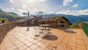 Una terraza con suelo de baldosas, mobiliario exterior y vistas a montañas.