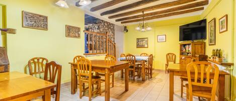 A dining area with wooden tables and chairs, a stone wall, and a television.