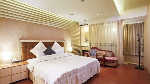 A hotel room with a large bed, a nightstand, a chair, and a window with curtains. - Wei Fengqing Motel (Tainan) (Tainan)