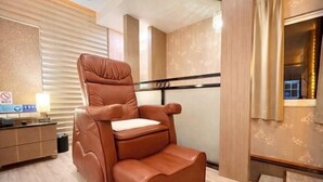 A massage chair in a room with a wooden floor, a small table with a lamp, and a window with curtains. - Wei Fengqing Motel (Tainan) (Tainan)