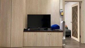 A room with a flat-screen TV on a wooden cabinet, a blue pillow, and a door leading to another room. - Wei Fengqing Motel (Tainan) (Tainan)