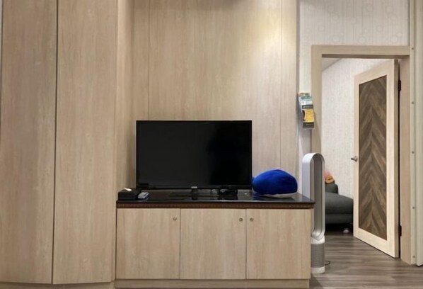 A room with a flat-screen TV on a wooden cabinet, a blue pillow, and a door leading to another room. - Wei Fengqing Motel (Tainan) (Tainan)
