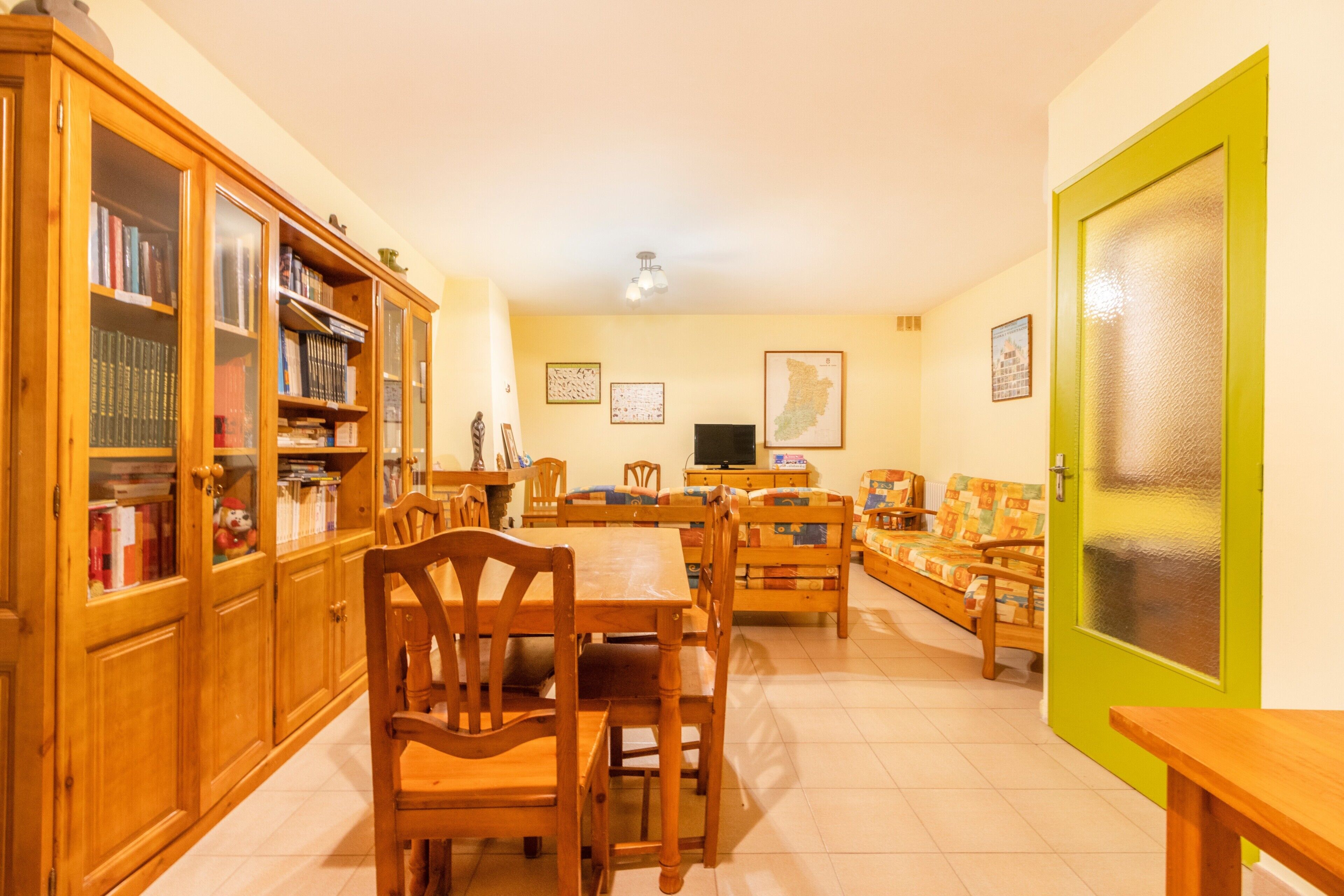 Una habitación con una mesa de comedor, sillas, un sofá, un televisor y un armario con libros.