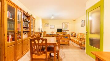 Una habitación con una mesa de comedor, sillas, un sofá, un televisor y un armario con libros.