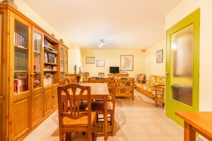 Une pièce comprenant une table à manger, des chaises, un canapé, un téléviseur et un meuble contenant des livres.