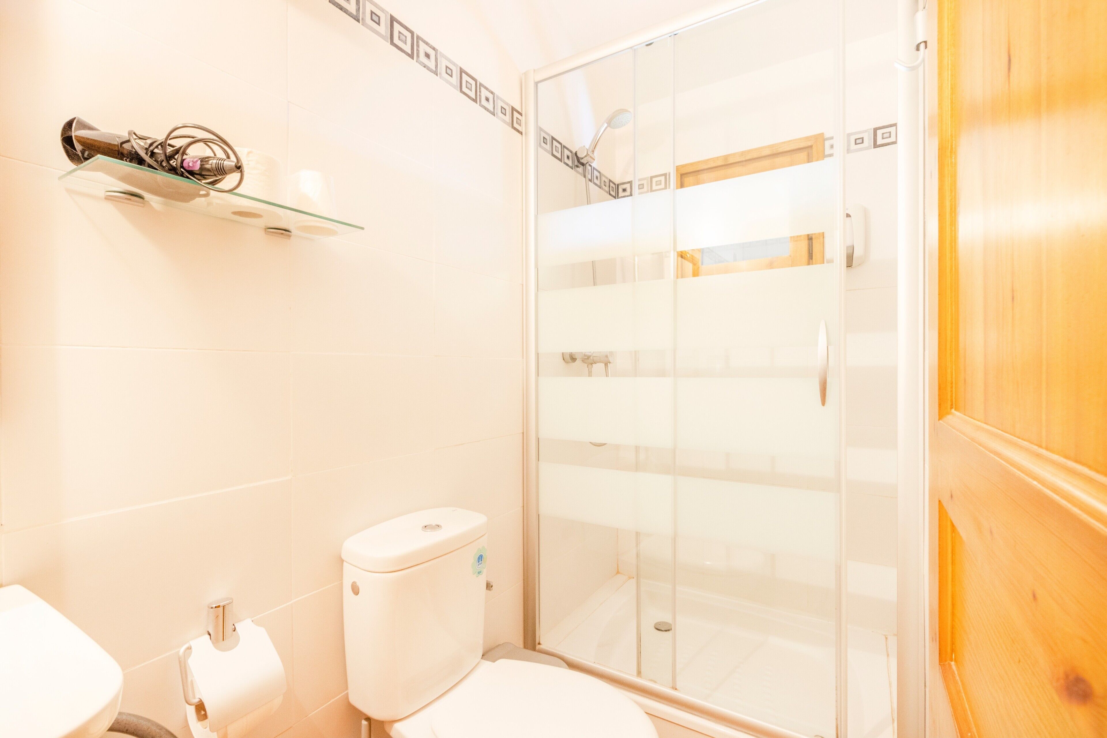 Et badeværelse med toilet, glasvæg til brusebad og en hylde med toiletartikler.