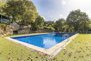 A rectangular swimming pool with clear blue water, surrounded by a stone wall and a grassy area with scattered leaves.
