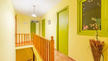 A hallway with a wooden railing, green doors, and a vase with dried plants.