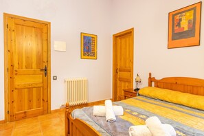 Une pièce avec des portes en bois, un lit recouvert d’une couverture jaune, un radiateur et un tableau encadré accroché au mur.