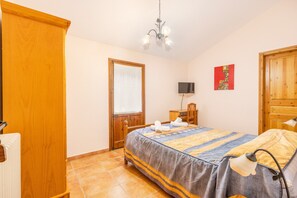Une chambre à coucher comprenant un lit, une armoire en bois, un bureau avec une chaise, une télévision et une porte.