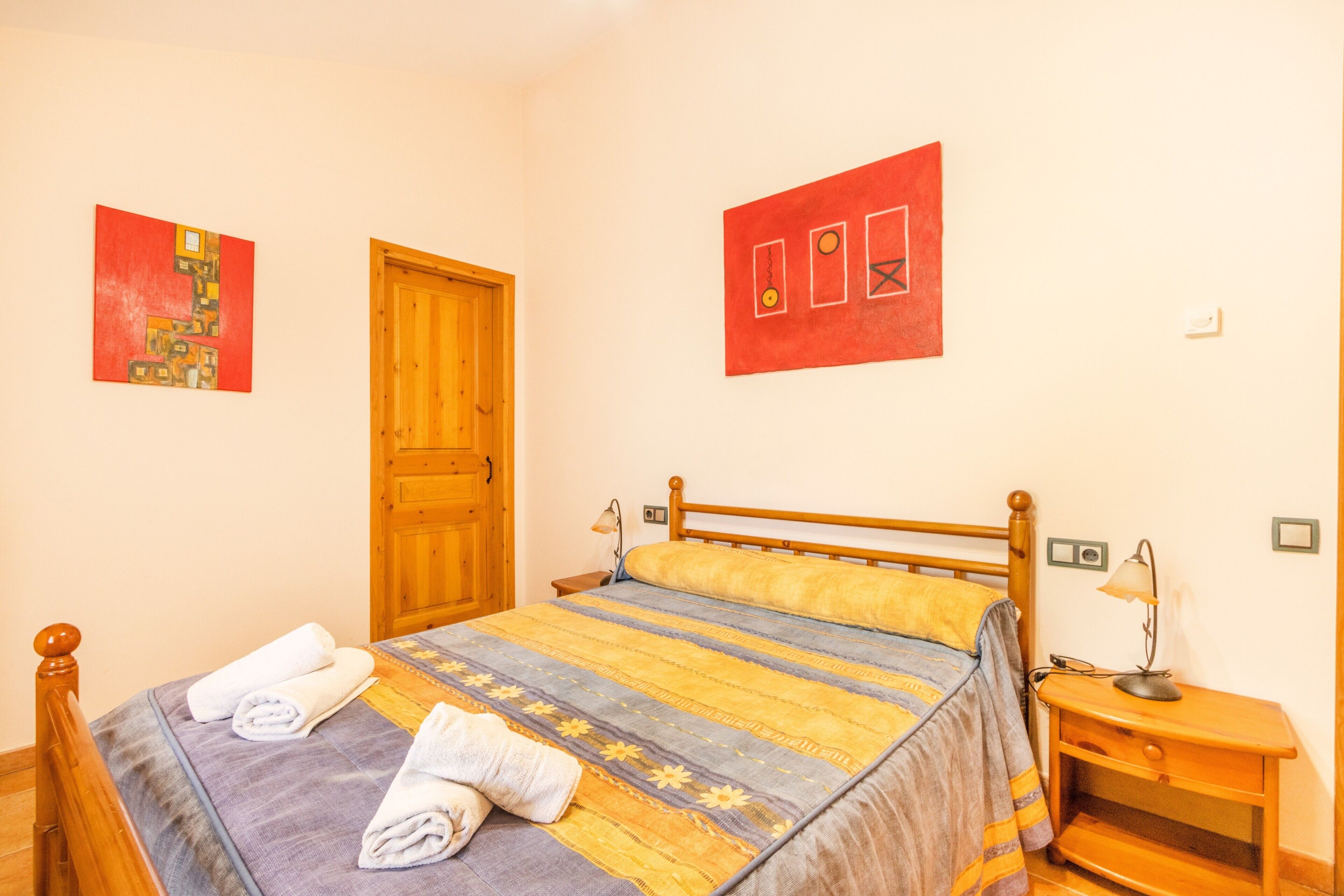 A bedroom with a wooden bed, a nightstand, a lamp, and two wall art pieces.