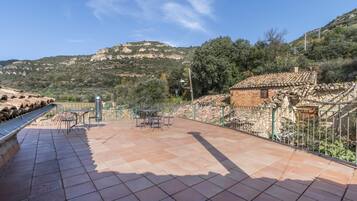 Eine Terrasse mit Tisch und Stühlen, ein kleines Backsteinhaus und eine gebirgige Kulisse.