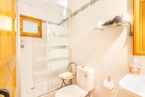 Une salle de bain avec une douche à parois de verre, des toilettes, un lavabo et une étagère contenant des articles de toilette.