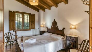 Quarto com cama de madeira, duas cadeiras, mesa de cabeceira e janela com persianas.