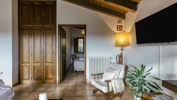 Una habitación con un armario de madera, un sillón mecedor blanco, una lámpara, un televisor y un radiador.