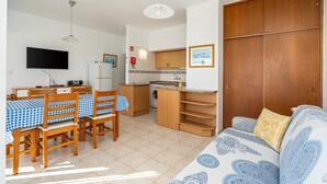 Un espace de vie compact comprenant un coin repas, une kitchenette et un canapé agrémenté d’un linge de lit à motifs.
