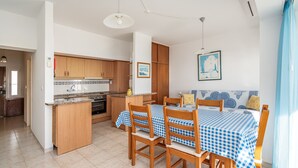 Une cuisine avec des meubles en bois, une table à manger recouverte d’une nappe à carreaux et une fenêtre donnant sur un beau paysage.