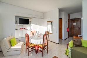 Een moderne woonkamer met een eettafel, stoelen, een bank en een aan de muur bevestigde televisie.