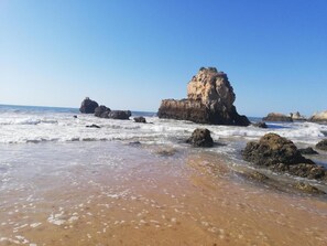 Une plage avec des formations rocheuses et un ciel bleu clair.