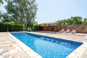 A rectangular swimming pool with clear blue water, surrounded by stone tiles.