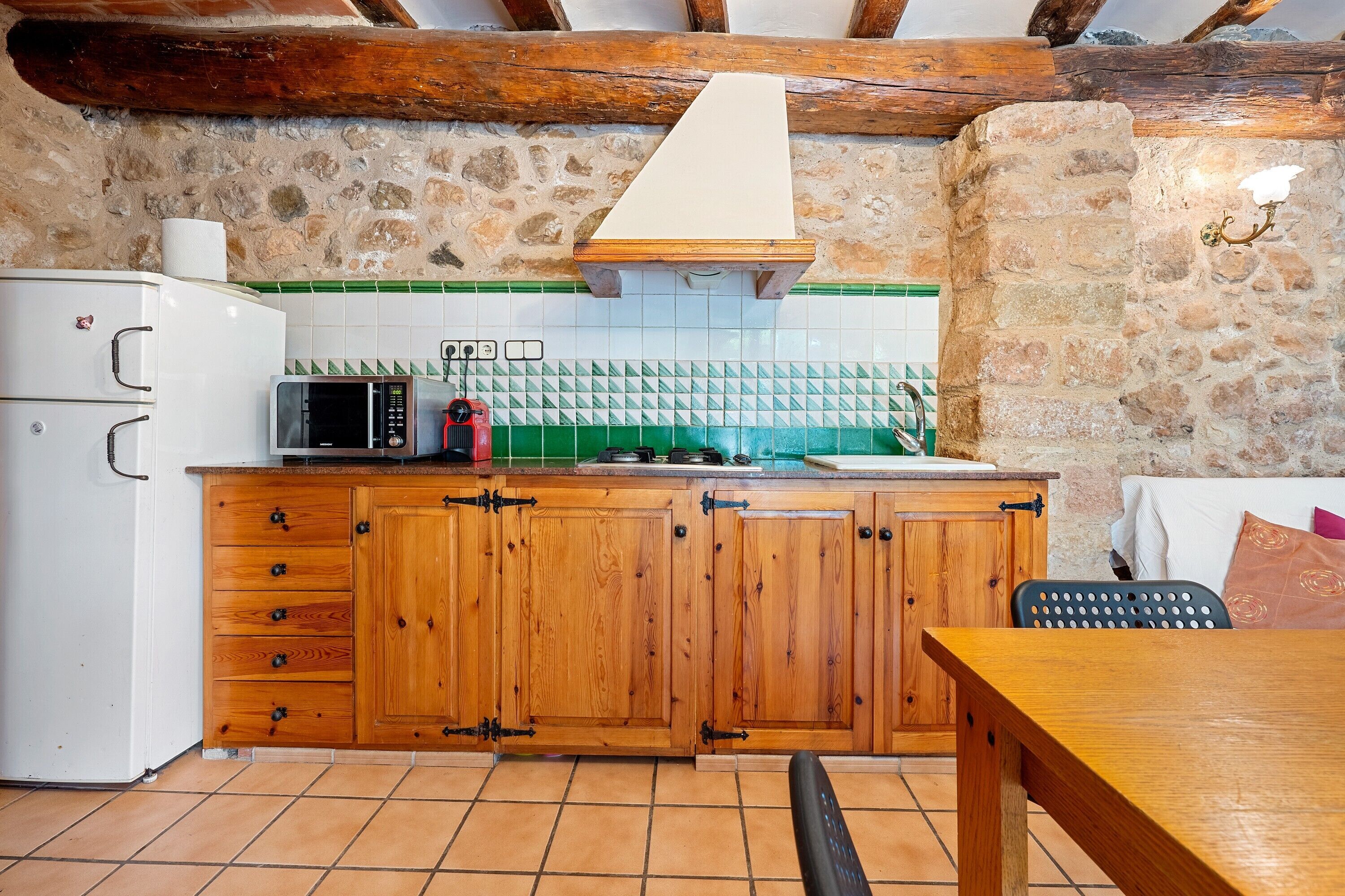 A rustic kitchen with wooden cabinets, a white refrigerator, a microwave, and a stove.