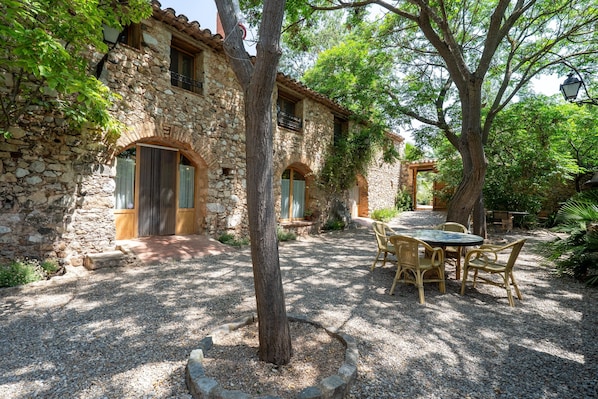 A stone building with a gravel patio, outdoor seating, and a tree in the center.