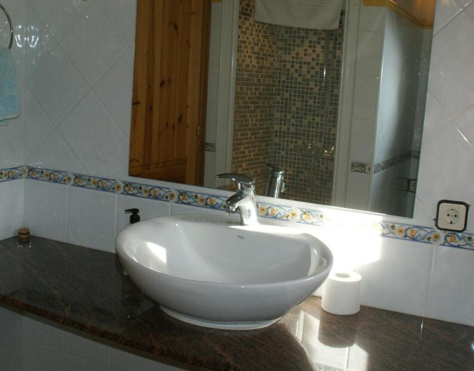 Un baño con un lavamanos blanco, un espejo y un rollo de papel higiénico.