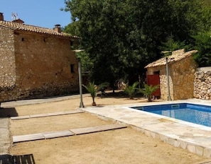 Un edificio de piedra con techo de tejas, piscina y un pequeño jardín.