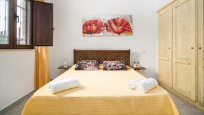 Une chambre d’hôtel comprenant un lit, deux oreillers, une table de chevet, une horloge murale et une grande armoire en bois.