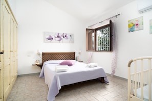 A bedroom with a bed, a window with curtains, a wooden headboard, and a wall-mounted artwork.
