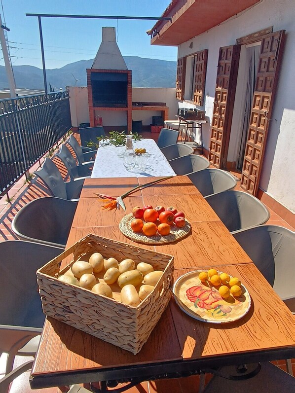 An outdoor dining area with a table set for two, a basket of potatoes, a plate of oranges, and a plate of lemons. - Holiday Home 'Chalet Venta Del Aire' with Mountain View, Wi-Fi and Air Conditioning (Lanjarón)