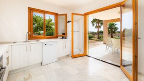 Una cocina moderna con lavavajillas, un lavamanos y una ventana que da a un patio con sillas.