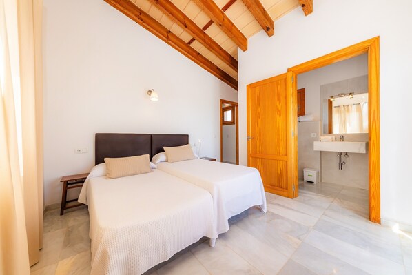 Un dormitorio con dos camas, techo de madera, baño con espejo y lavamanos, y puerta de madera.