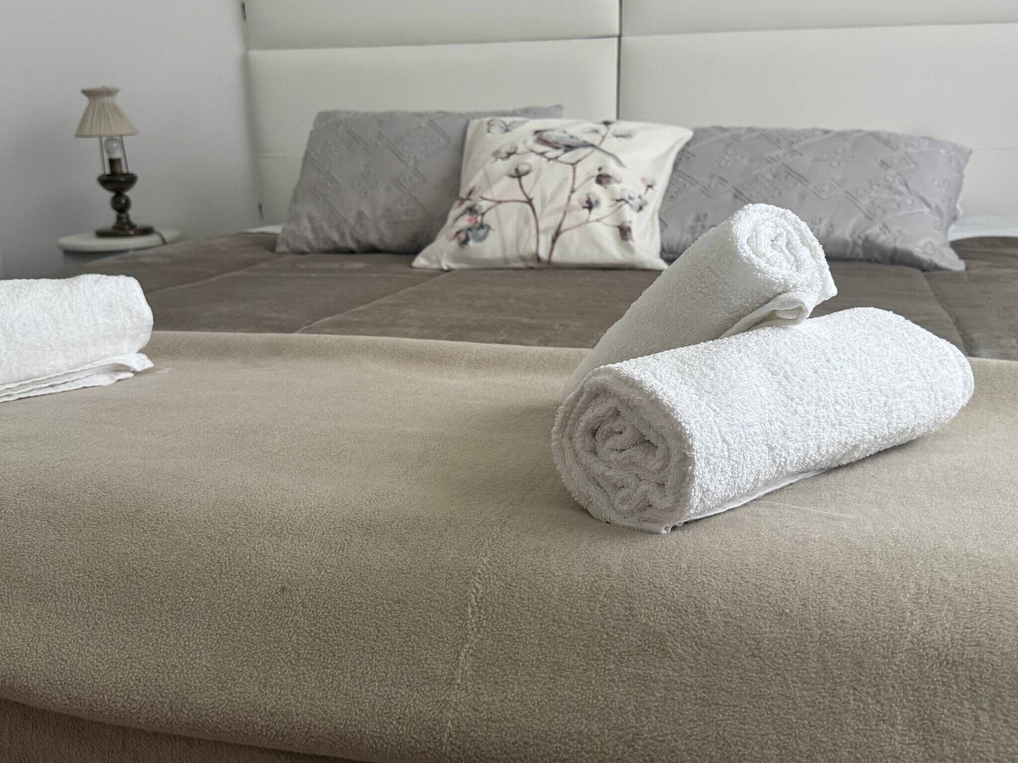 Een net opgemaakt bed met een beige deken en opgerolde witte handdoeken.