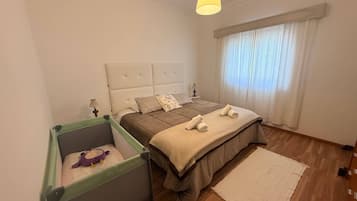 Et soveværelse med seng, sengebord, lampe, et vindue med gardiner og en lille grøn legevæg med en legetøj.