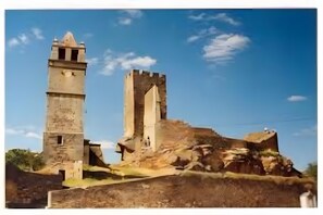 A historic stone tower and a castle ruin with a clear sky.
