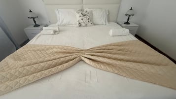 Una cama bien tendida con un edredón acolchado, dos mesitas de noche con lámparas y un cabecero.