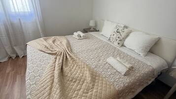 Une chambre à coucher comprenant un lit, une table de chevet, une lampe, une fenêtre avec des rideaux et un tableau accroché au mur.