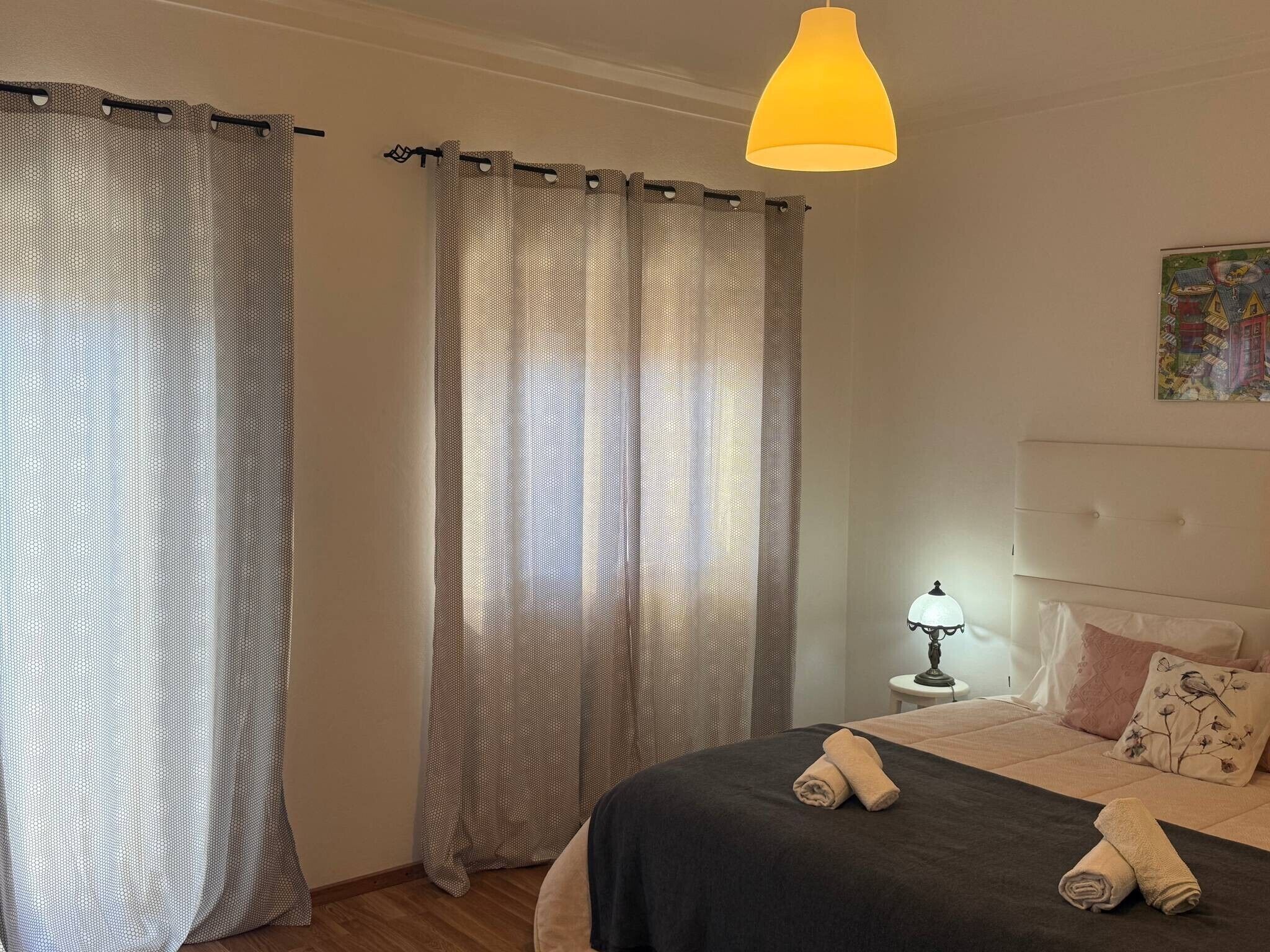 Una habitación de hotel con cama, mesita de noche con lámpara y un cuadro en la pared.
