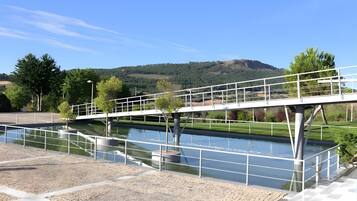A bridge over a canal with a clear sky, trees, and a hilly landscape in the background.