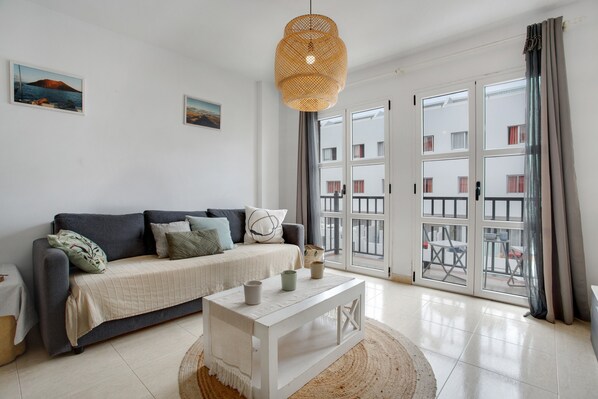 A living room with a sofa, a coffee table, a hanging light fixture, and a view through a glass door.