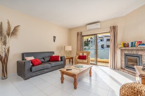 A living room with a sofa, a coffee table, a fireplace, and a view of the outside. - Apartment 'Norah’s House' with Shared Pool, Wi-Fi and Air Conditioning (Carvoeiro)