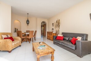 A living room with a sofa, a coffee table, a wicker chair, a dining table with chairs, and a cabinet. - Apartment 'Norah’s House' with Shared Pool, Wi-Fi and Air Conditioning (Carvoeiro)