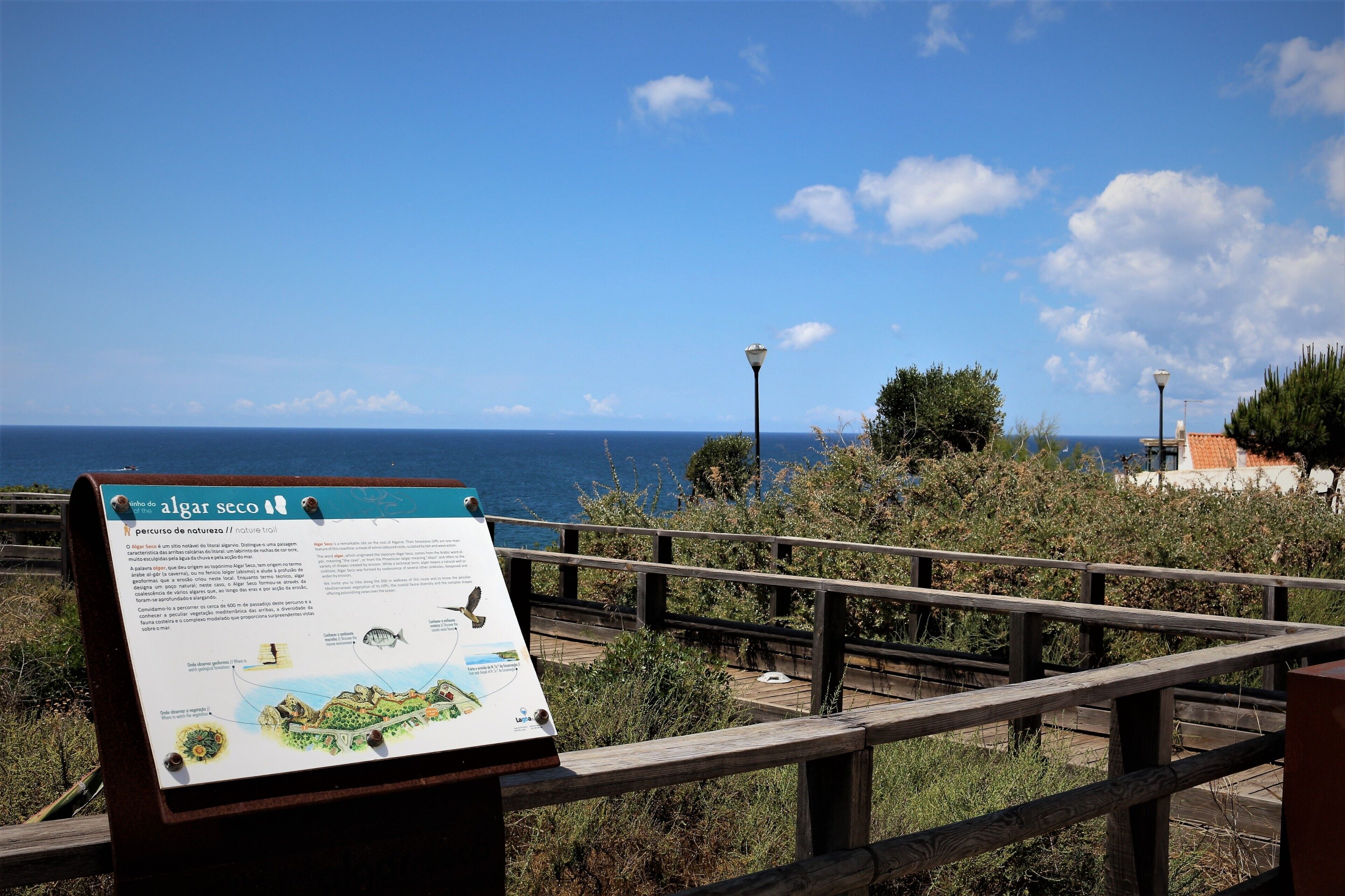 Une promenade en bois, agrémentée d’un panneau d’information sur Algar Secco, qui offre une vue sur la mer.