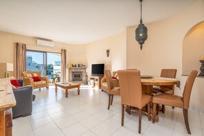 A living room with a fireplace, television, dining table, and chairs. - Apartment 'Norah’s House' with Shared Pool, Wi-Fi and Air Conditioning (Carvoeiro)
