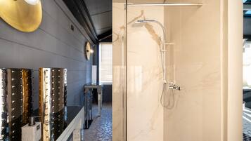 Une salle de bain moderne dotée d’une douche à parois de verre, de murs en marbre et d’un mur réfléchissant agrémenté d’éléments métalliques.