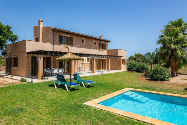 Una casa de dos pisos con piscina, mobiliario exterior y un césped bien cuidado.