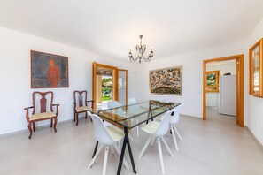 Un comedor con mesa de vidrio, sillas blancas, sillas de madera, una araña y obras de arte en las paredes.