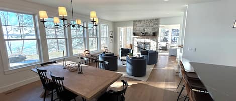 A spacious dining area with a wooden table and chairs, a stone fireplace, and large windows offering a view of the outdoors.