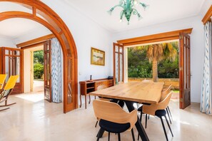 Un vaste espace dédié à la salle à manger, avec une grande table et des chaises en bois, un lustre et une vue sur l’extérieur.